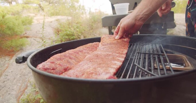 A rack of dry rubbed ribs being slow cooked and smoked on a kettle grill barbecue