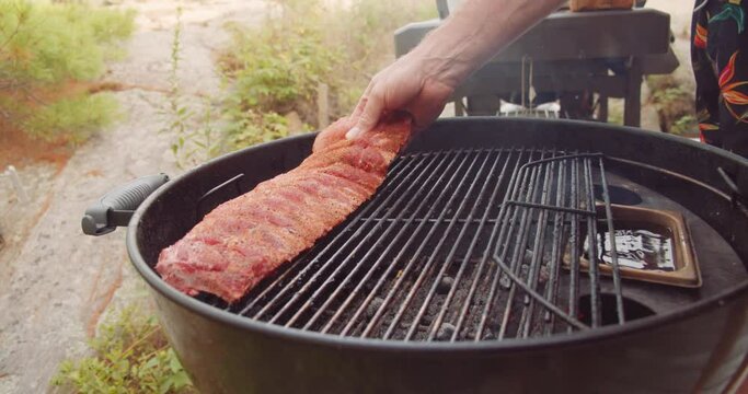 A rack of dry rubbed ribs being slow cooked and smoked on a kettle grill barbecue
