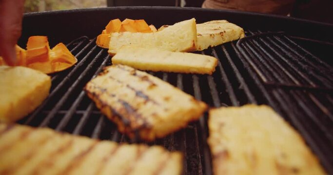 Fresh mango, pineapple slices and a wheel of brie cheese in a ramekin being placed on a barbecue grill