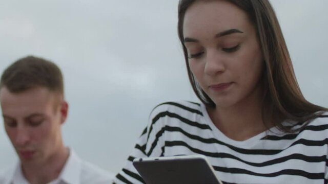 Two girls and a guy sitting in the park during the day reading an e-book