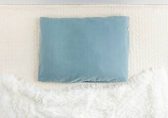 Above view of blue pillow and white soft blanket on bed. Minimal bedroom background, copy space.