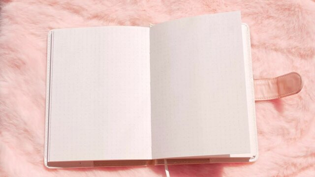 Blank notebook mockup on pink faux fur flat lay. Coral fluffy feminine fabric background top view. Female blog rose textile surface notepad copy space text sign design. White sketchbook sheet template