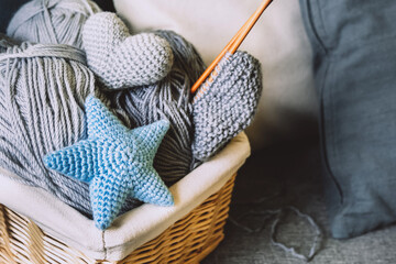 Gray balls of wool and knitting needles in wicker basket on gray sofa with pillows. Home hobby, knitting, decorative knitted toys