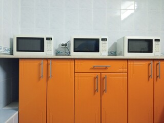 
In the dining room, there are three microwave ovens on the orange-colored kitchen set
