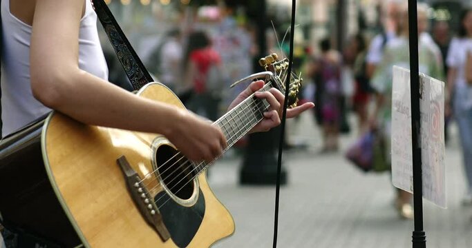 A young street musician plays an acoustic guitar on a city street.