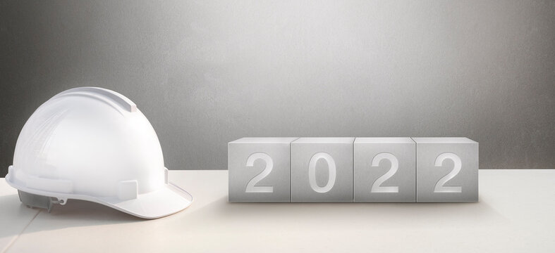 Happy New Year 2022 Construction and Industry.White Helmet and a numbered concrete cube on the desk of an engineer or construction worker.