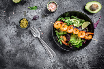 Vegetarian vegetable low carb lunch bowl with avocado, fresh salad, grilled shrimps and pesto sauce. Healthy diet seafood concept. Top view