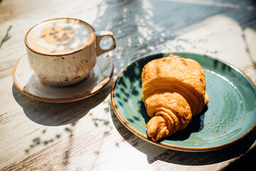 Cappuccino and croissant are on the table in the cafe. Morning sunlight falls on the table, beautiful shadows appear.