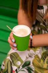 Coffee latte to go in green paper cup in a young girl hand