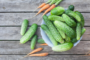 on a wooden table there is a bowl of cucumbers. Nearby lies a young small carrot.