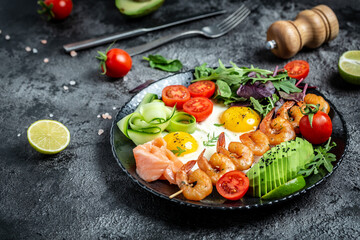Ketogenic breakfast. Keto low carb salmon, grilled shrimps, prawns, fried eggs, fresh salad, tomatoes, cucumbers and avocado. keto diet. Top view