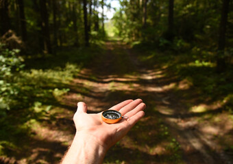 Compass in hand at road in the forest. Tourist compass for orientation on the terrain. Magnetic...
