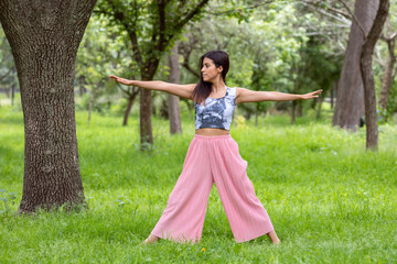 Latin woman doing Yoga-asanas with different postures, in the outdoor park with grass and trees in the background