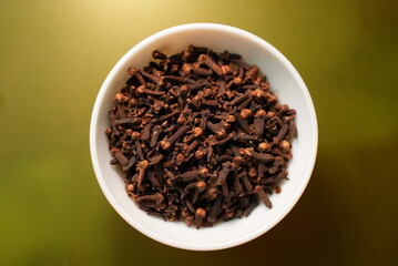 Some dry roasted cloves  on a ceramic bowl on top of green background 