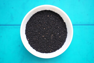 Some black cumin seed grains on a clay bowl on top of blue background texture 
