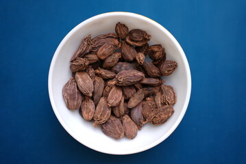 Some Dried Cardamom on a ceramic bowl on top of blue background