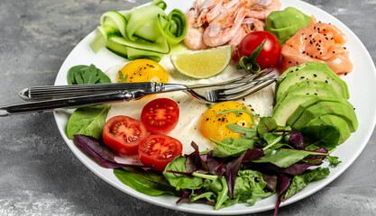 Ketogenic breakfast. Keto low carb salmon, boiled shrimps, prawns, fried eggs, fresh salad, tomatoes, cucumbers and avocado. Top view