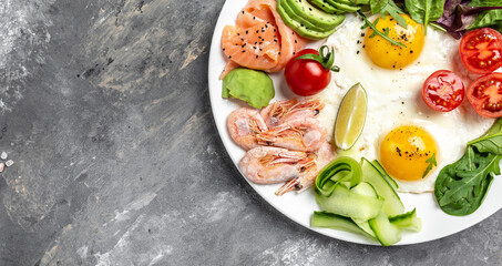 Ketogenic breakfast. Keto low carb salmon, boiled shrimps, prawns, fried eggs, fresh salad, tomatoes, cucumbers and avocado. Top view