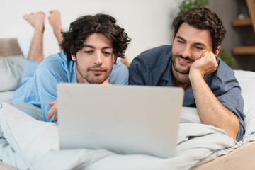 happy gay couple watching movie on laptop in bedroom