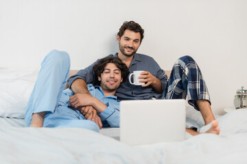 happy gay couple watching film on laptop in bed