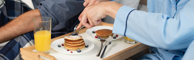 cropped view of gay couple having breakfast in bed, banner