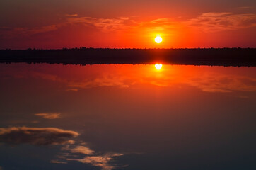 Naklejka na ściany i meble Beautiful sunrise on the lake. The sun rises above the horizon. Early morning, calm water.