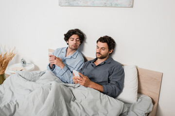 man looking at mobile phone while boyfriend texting in bed