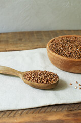Buckwheat in a wooden tablespoon with a bowl on a linen napkin on a wooden table. Rustic style. Healthy nutrition concept. Horizontal orientation. Selective focus.