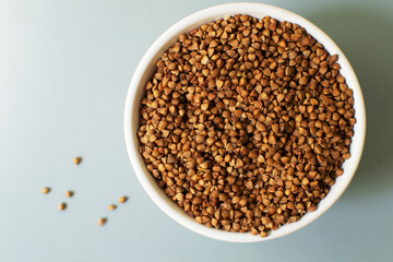 Dry buckwheat lies in a white bowl on a gray background. Healthy nutrition concept. Horizontal orientation. Buckwheat contains a large amount of vitamins and minerals. Top view. Copy space.