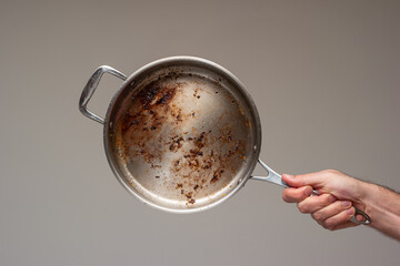Dirty oily burnt metal frying pan held in hand by male hand. - obrazy, fototapety, plakaty