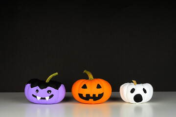 Painted Halloween pumpkins on a white shelf against a black background. Monster, Jack o Lantern and...