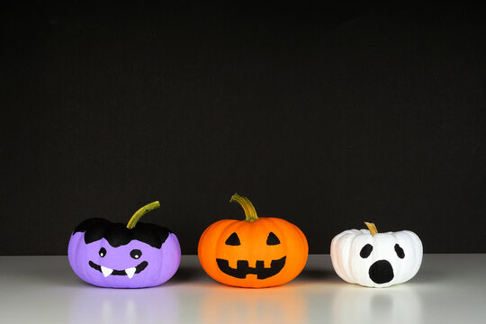 Painted Halloween pumpkins on a white shelf against a black background. Monster, Jack o Lantern and ghost.
