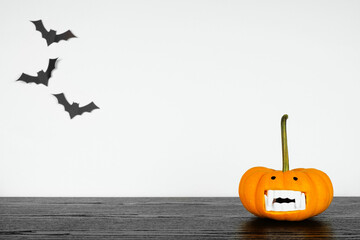 Halloween pumpkin with vampire teeth on a black shelf against a white wall with bats. Copy space.
