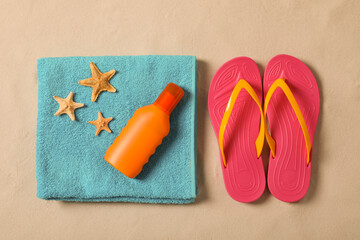 Beach towel, sunscreen, starfishes and flip flops on sand, flat lay