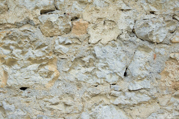 Frontal view of a wall made of brown-yellow rough rough stones of irregular shape and different sizes fastened with cement