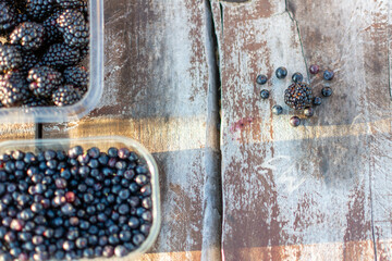 Plastic bowls of fresh blackberries and blueberries on a wooden table, top view, horizontal, copy space.