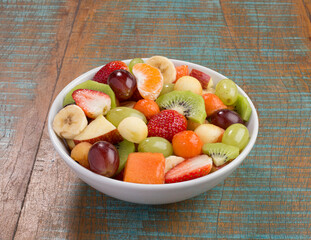 Deliciosa salada de frutas em tijela branca sobre mesa de tampo rústico.