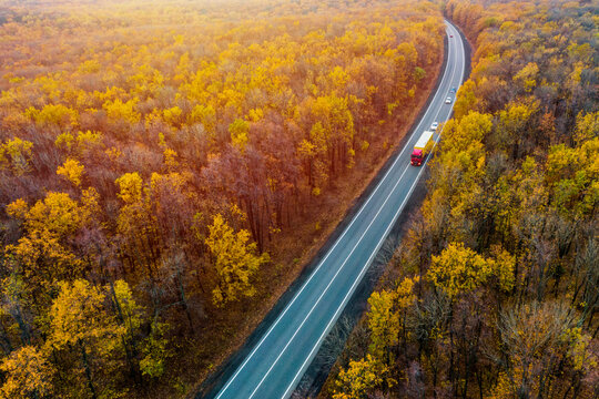 red truck drives on an asphalt road along  the autumn forest. cargo transportation. Cargo delivery at Sunset. Top view. Drone photo