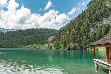 A boat shed and a view to an emerald green Blindsee lake surrounded by forest and mountains