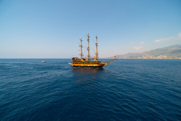 Fototapeta na wymiar Old pirate ship on the water of Mediteranean sea. Tourist entertainment, coastal tour. Summer sunny day. Mountain shore of Alanya. Turkey.