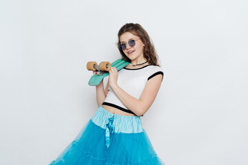 Happy stylish girl teenager in sunglasses posing with penny board on white background