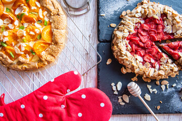 Apricot and strawberry galette placed on wooden table with cooking tools on the side.