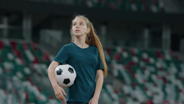 ZOOM OUT Caucasian pre teen girl entering the field of huge soccer stadium, holding a ball, dreaming of becoming professional player, soccer star