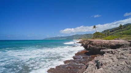 View of the volcanic cliffs on the tropical beach of Oahu Hawaii. Waves crash against the sharp edges of the stones. Cinematic 4K wildlife. Untouched nature on a sunny summer day. DCI.