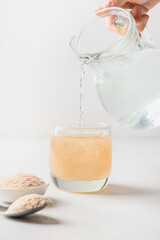 Woman pouring water glass with psyllium fiber on a white background. Superfood for healthy...