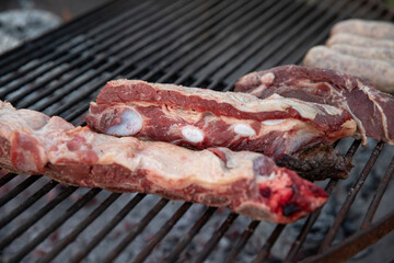 Traditional asado outdoors. Barbecue. Closeup view raw red meat grilling outside. 