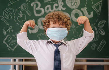 a little boy in a medical mask on the background of a blackboard with the text back to school