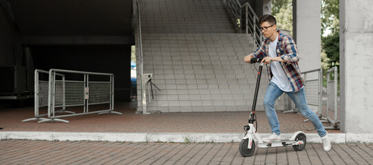 A young businessman in a shirt and glasses starts riding an electric scooter. The modern entrepreneur uses modern ecological transport