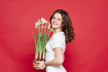 Portrait of an attractive young woman in summer clothes holding potted blooming flowers over red background