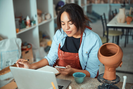 Charming female potter using laptop and smartphone in workshop